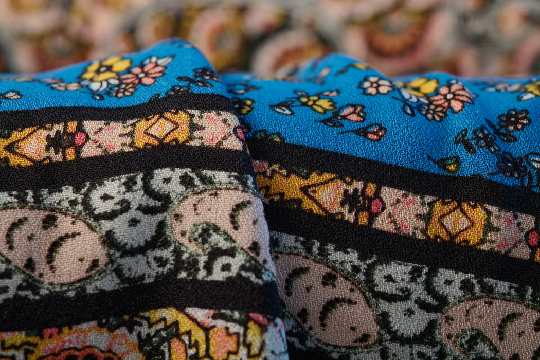 Blue, pink, black, and yellow colored crepe fabric with a flower and paisley print made from rayon.